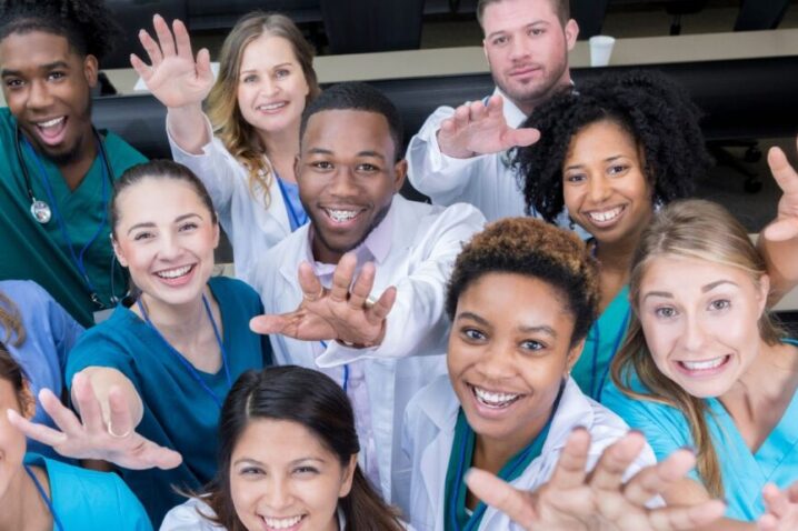 A multi-disciplinary team of health care providers waving at the camera